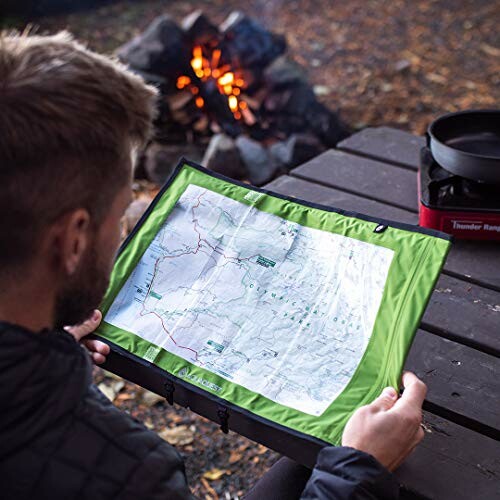 Person holding a map at a campsite with a fire and cooking gear.